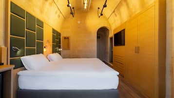 A modern bedroom with a large bed, built-in wooden cabinets, and a stone wall.