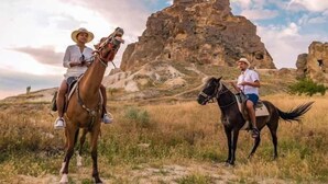Two people riding horses in a natural landscape with rocky formations in the background. - Uchisar Kaya Hotel - Special Class (Nevsehir)