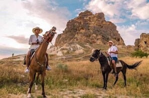 Two people riding horses in a natural landscape with rocky formations in the background. - Uchisar Kaya Hotel - Special Class (Nevsehir)