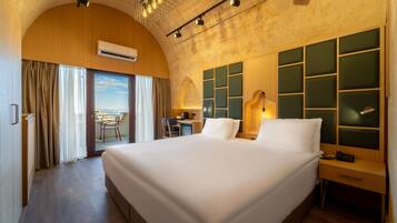 Habitación de hotel con una cama grande, un escritorio con silla, vista a través de un ventanal y un diseño moderno en el techo.