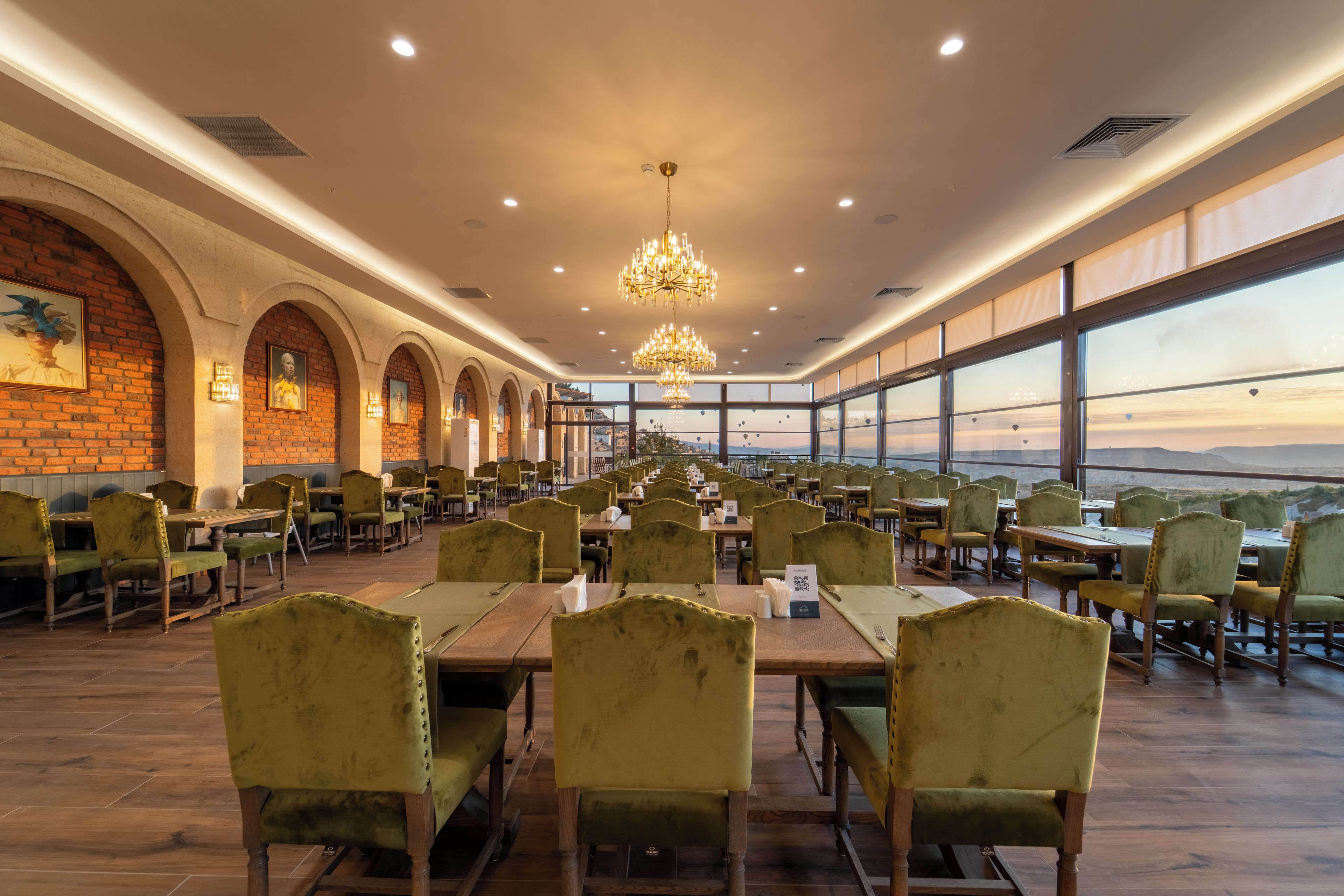 A restaurant with a long table layout, arched brick walls, and a view through large windows.