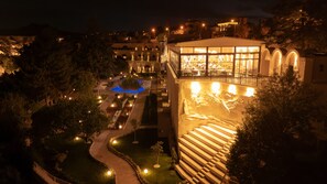 A nighttime view of a hotel with a pool, outdoor seating area, and a staircase leading to the upper floors. - Uchisar Kaya Hotel - Special Class (Nevsehir)