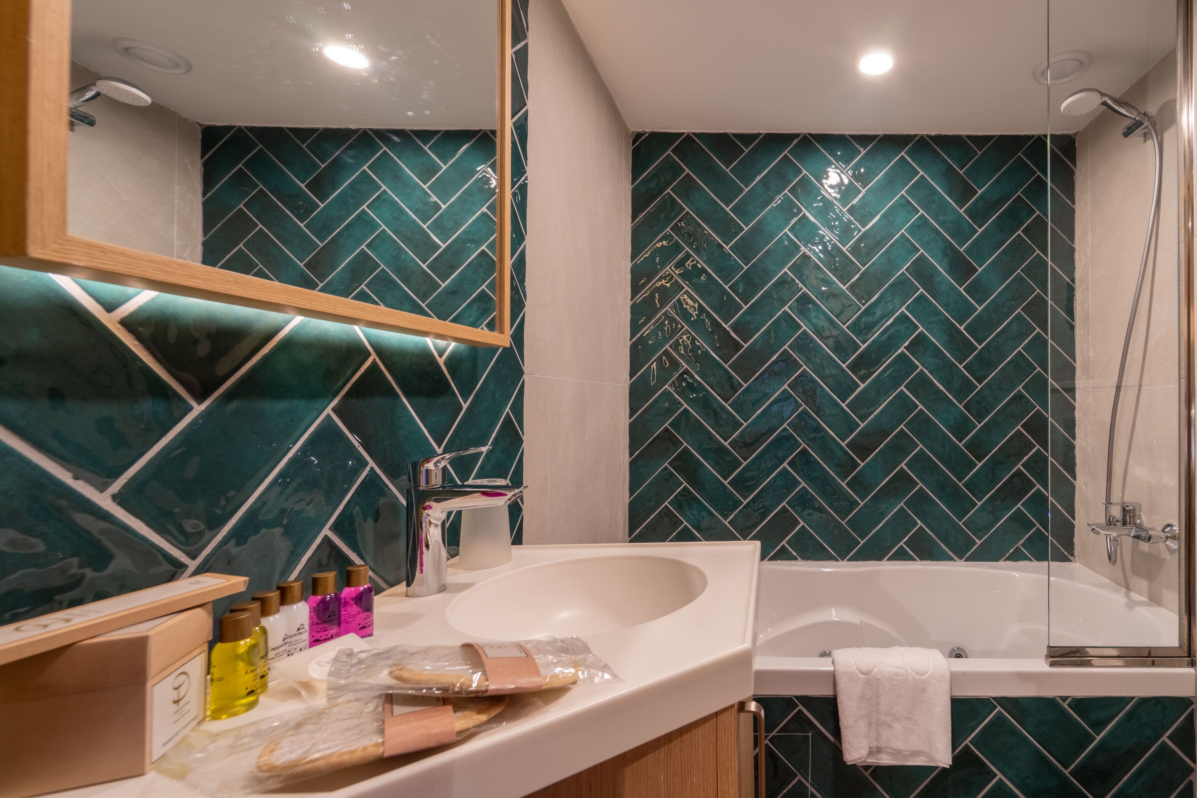 Casa de banho com uma pia branca, um espelho, chuveiro e parede de azulejos em padrão herringbone.