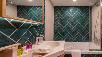 Casa de banho com uma pia branca, um espelho, chuveiro e parede de azulejos em padrão herringbone.