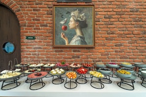 Een buffet met diverse gerechten, een schilderij aan de muur en een bord dat het keukenareaal aangeeft.