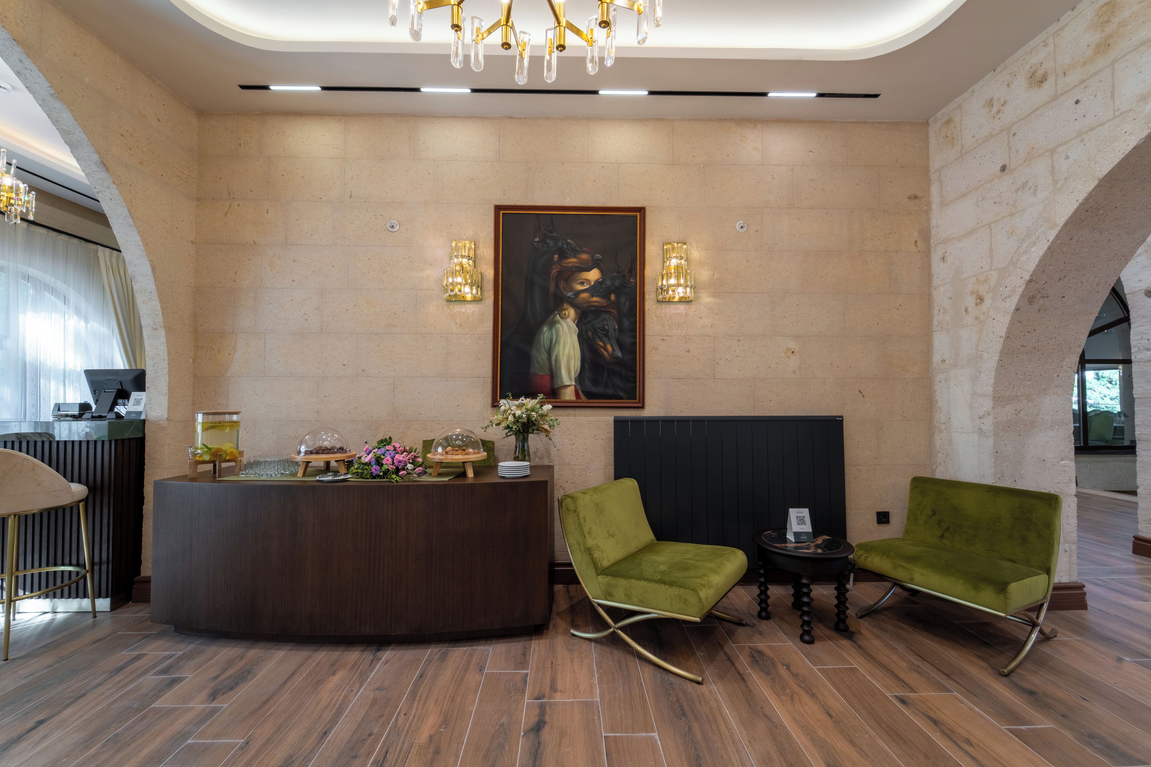 Uma área de recepção com balcão de madeira, duas poltronas verdes, um quadro na parede e um lustre.