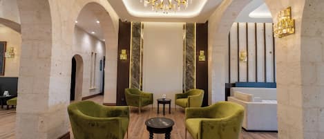 Un vestíbulo con candelabro, sillones tapizados en verde, mostrador de recepción y detalles de mármol.