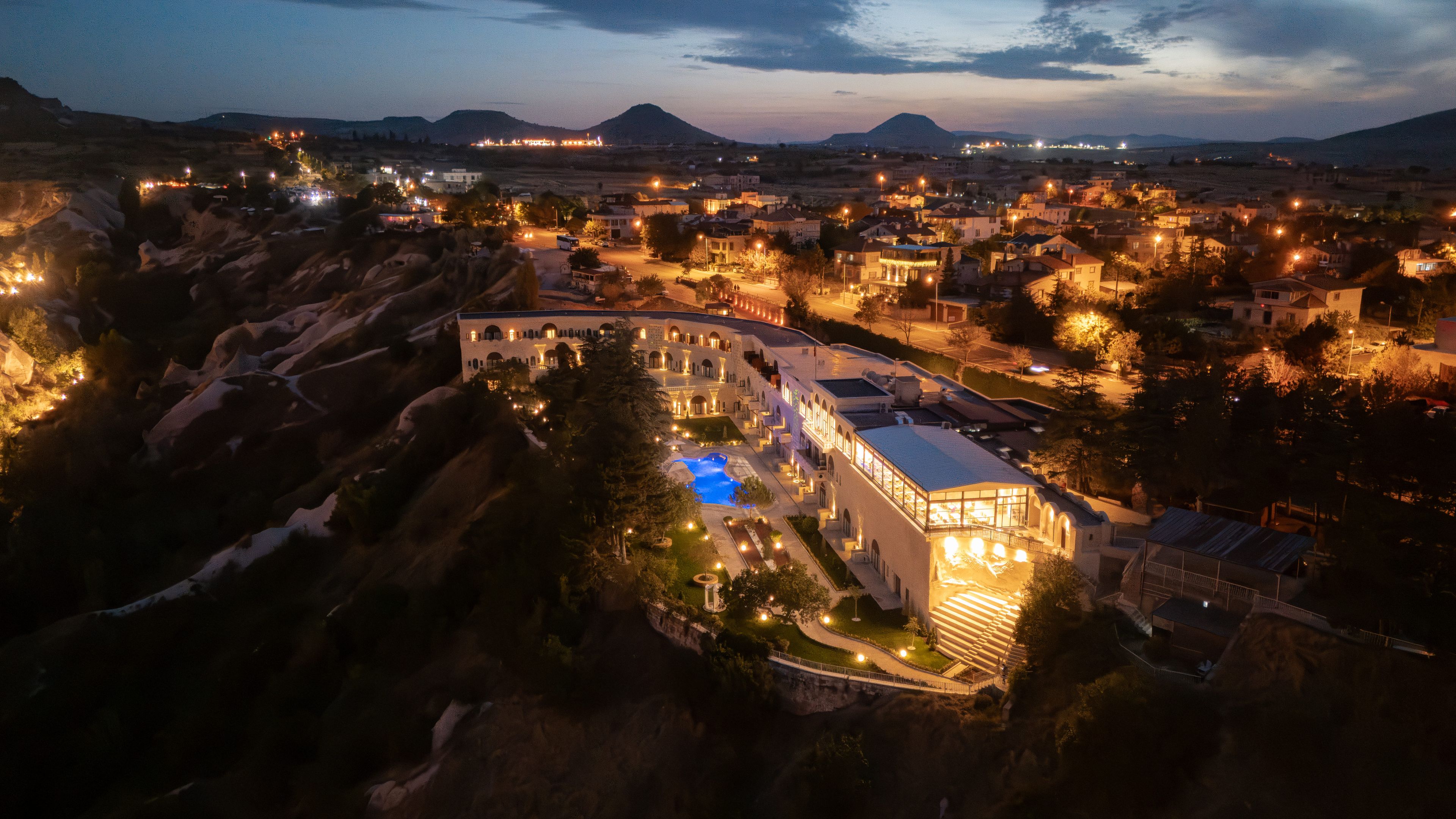 A large hotel with multiple buildings, a swimming pool, and a mountainous backdrop.