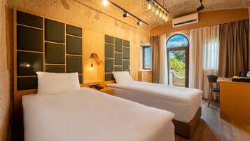 Quarto de hotel com duas camas, uma escrivaninha, uma luminária e vista para o verde.