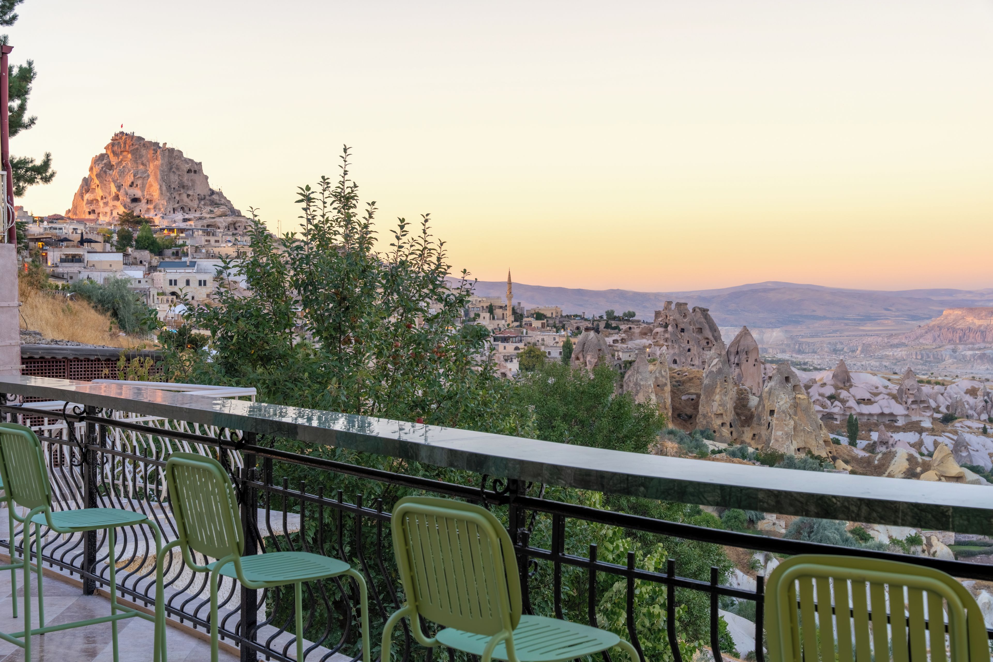 Una terraza con sillas verdes que da a una vista panorámica de la ciudad, con formaciones rocosas características y una mezquita.