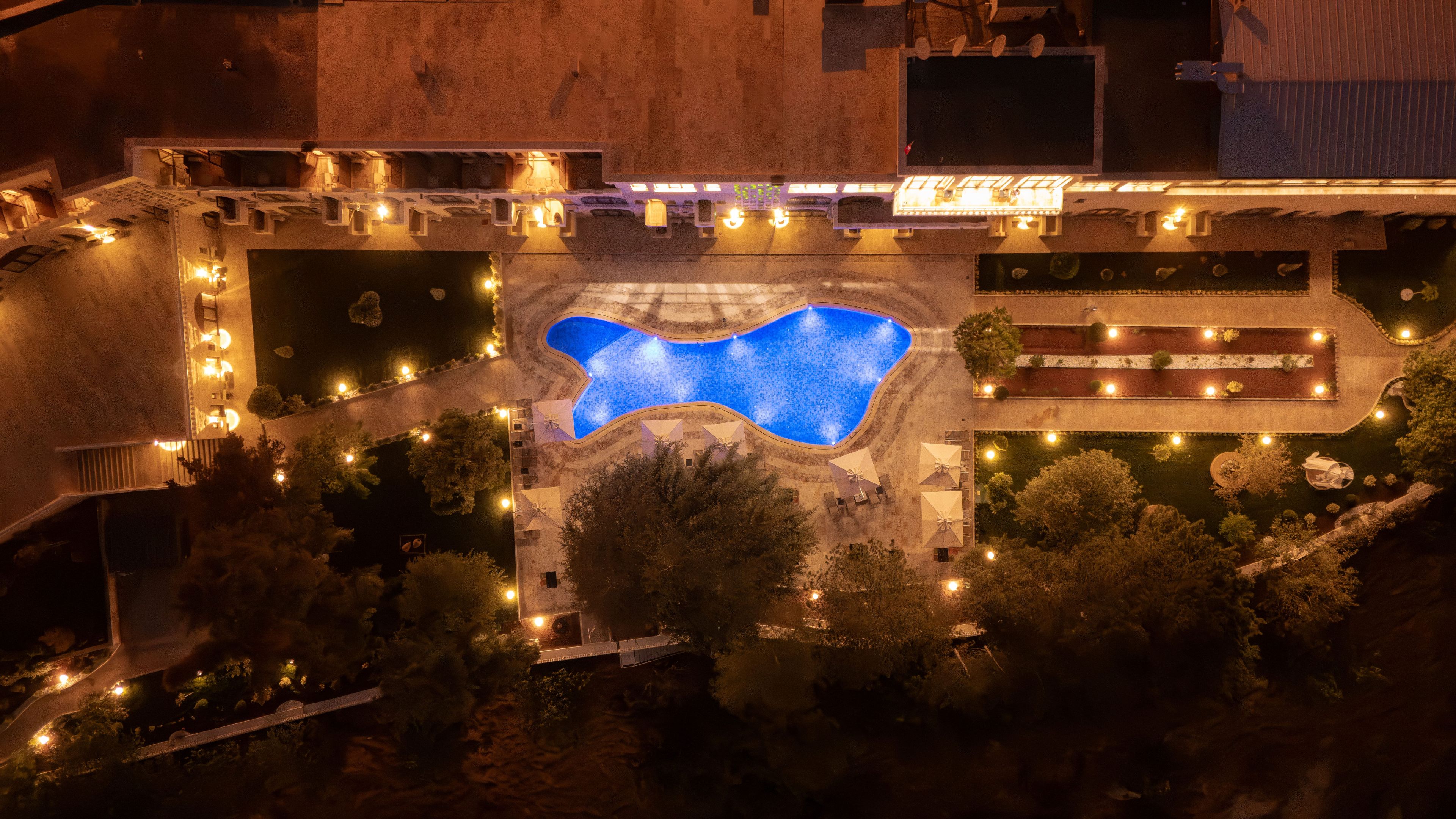 Vue aérienne d’un complexe hôtelier doté d’une piscine centrale, entourée de jardins aménagés et d’espaces de détente en plein air.