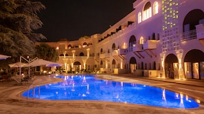 A nighttime view of a hotel with a swimming pool, outdoor seating, and a multi-story building with arched windows and balconies. - Uchisar Kaya Hotel - Special Class (Nevsehir)