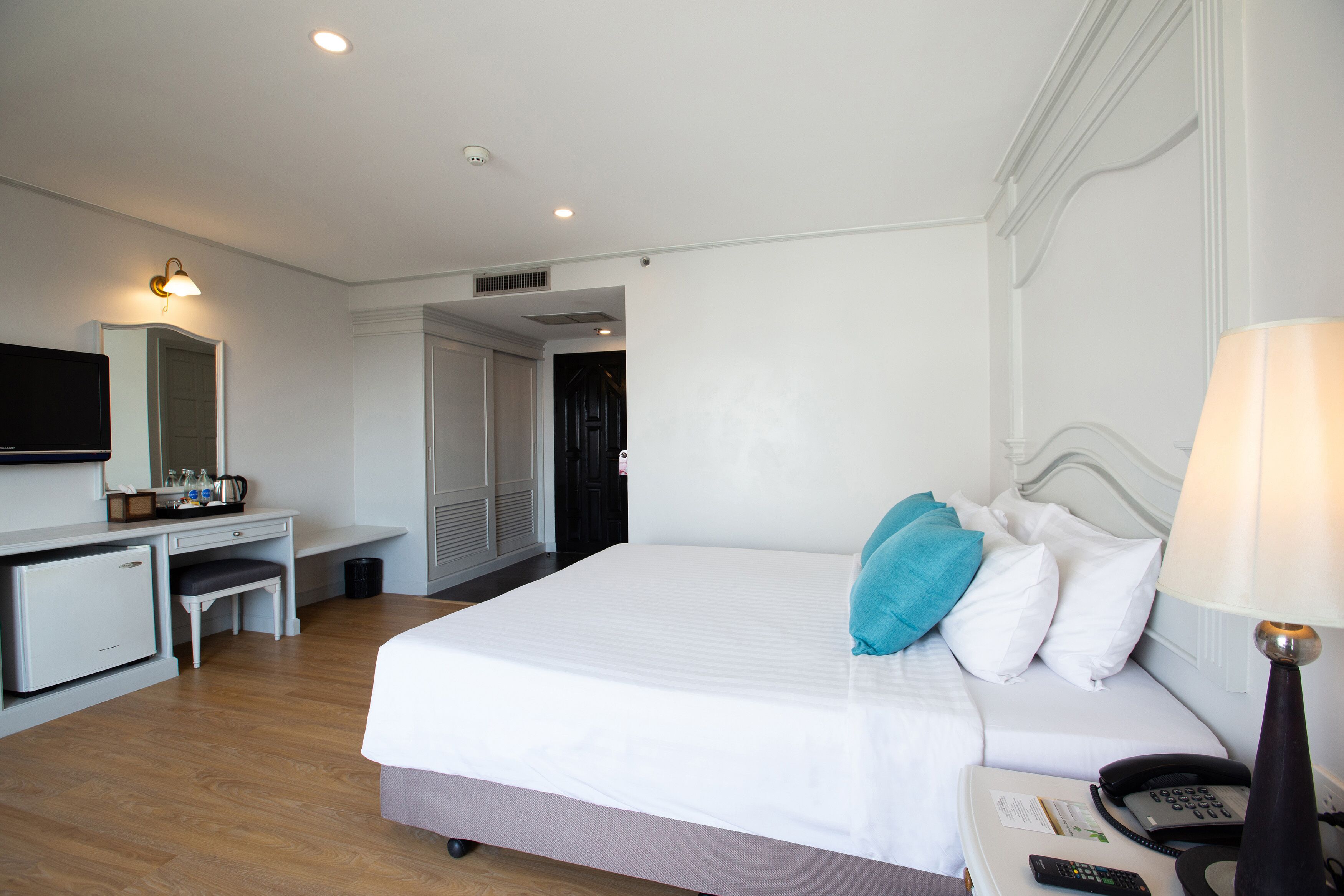 A hotel room with a bed, bedside table, lamp, desk with a chair, and a small refrigerator.