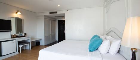 A hotel room with a bed, bedside table, lamp, desk with a chair, and a small refrigerator.