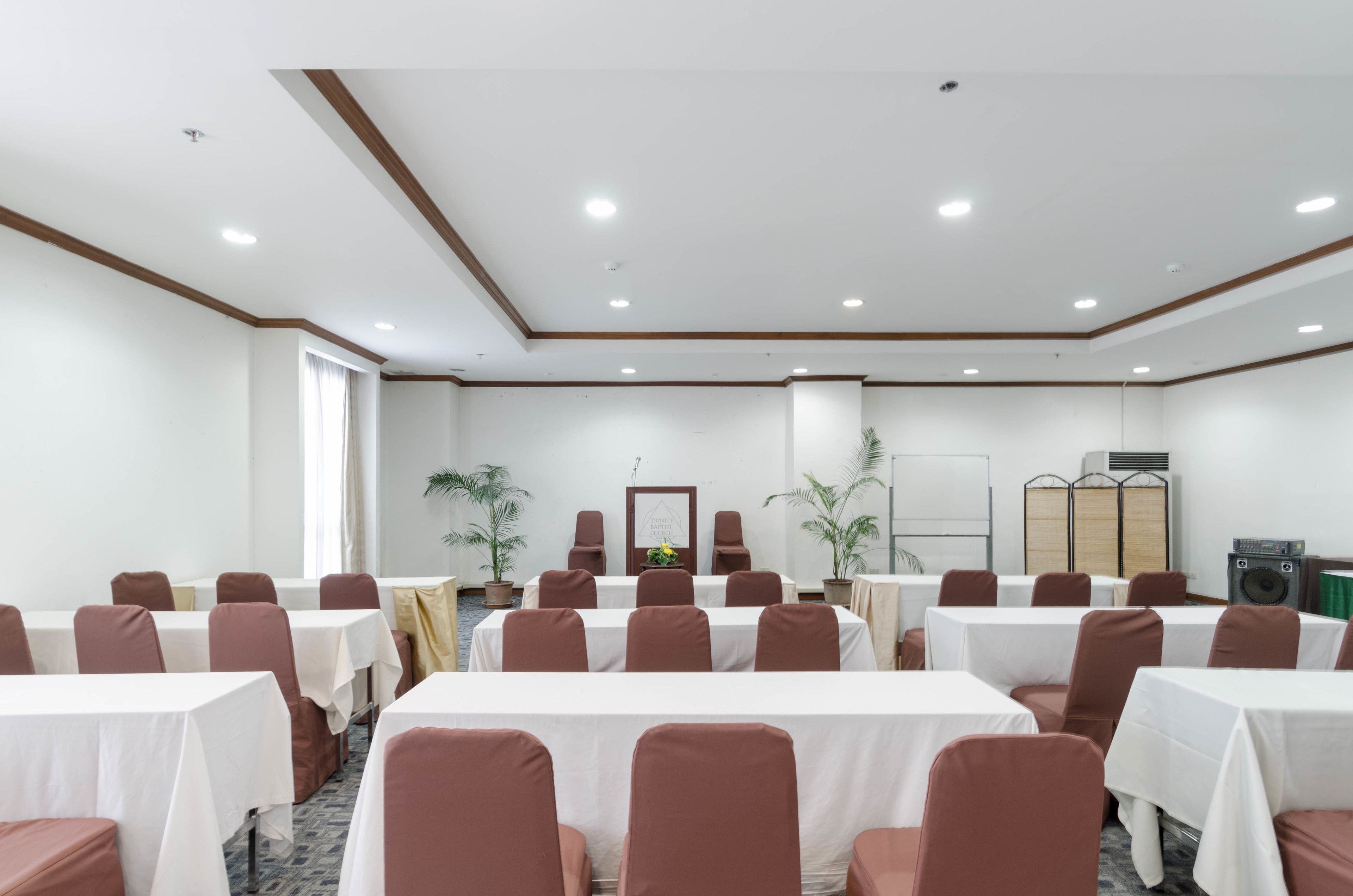 A conference room with multiple tables and chairs, a whiteboard, and a speaker system.