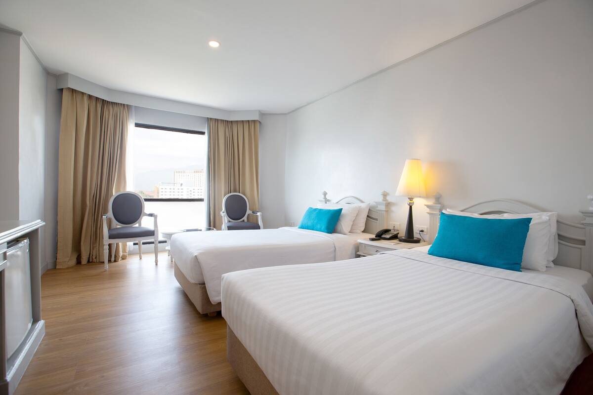 A hotel room with two beds, a desk, and a chair.