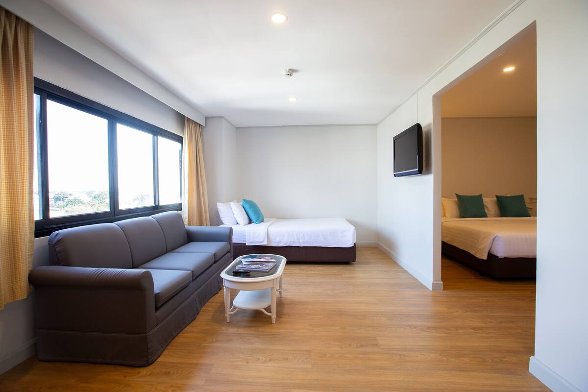 A modern hotel room with a sofa, a small table, a bed, and a TV mounted on the wall.