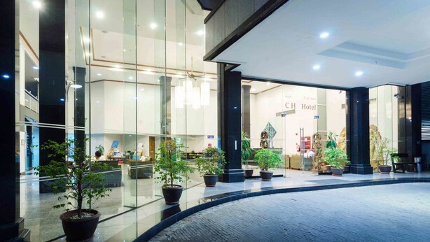 Entrada de hotel con puertas de vidrio, plantas en macetas y una recepción.
