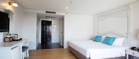 A hotel room with a bed, bedside table, and a desk with a chair. There is a mirror on the wall and a door leading to another room.