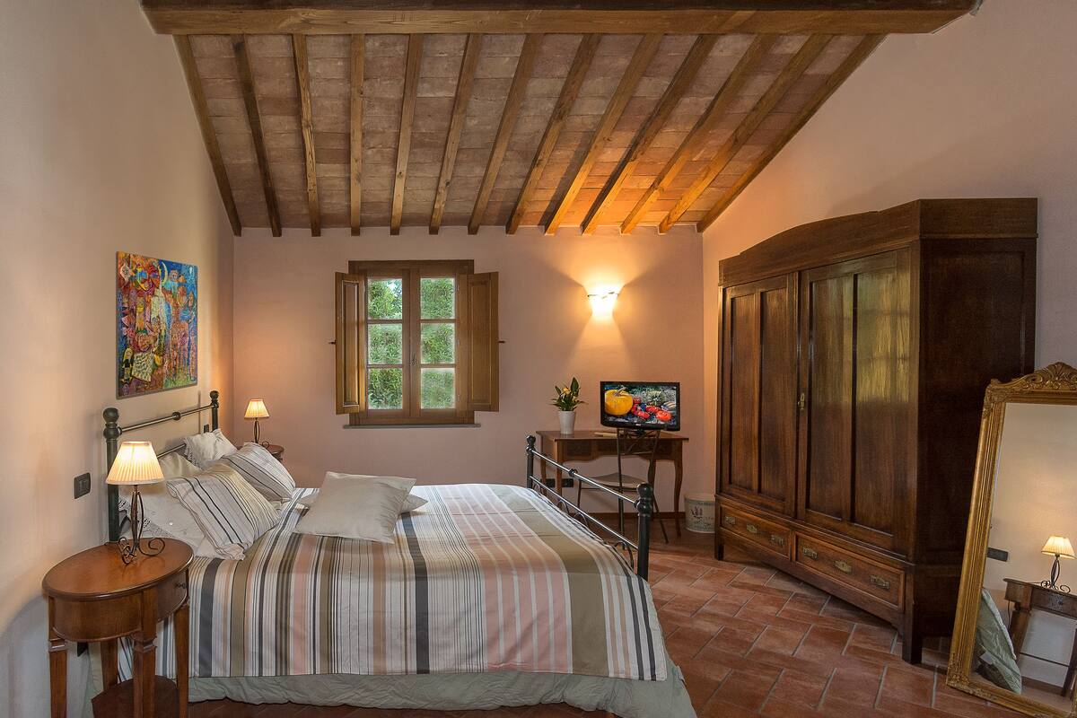 A bedroom with a bed, bedside tables, a television, a wardrobe, and a window with natural light.