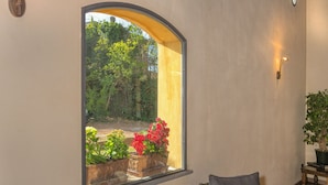 Una habitación con muebles de mimbre, un ventanal con vistas a la vegetación y una lámpara fijada a la pared.