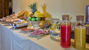 Una mesa de buffet con diversos alimentos, como frutas, pasteles y carnes, junto con varias botellas de bebidas.