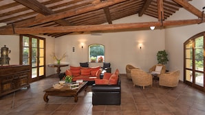 Amplia sala de estar con techo de madera alto, chimenea, un conjunto de sofás y sillones de mimbre.