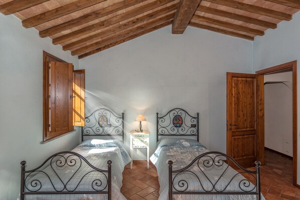 A bedroom with two beds, wooden ceiling beams, a nightstand with a lamp, and a wooden door.
