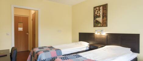 A hotel room with two single beds, a desk, and a chair.