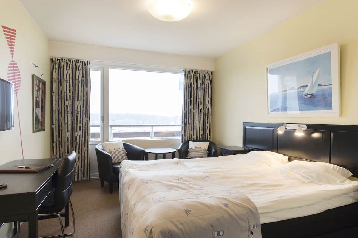 A hotel room with a bed, a desk, a chair, a small table, a TV, and a window with curtains.