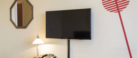 Habitación de hotel con escritorio, televisor de pantalla plana en la pared, teléfono y lámpara.