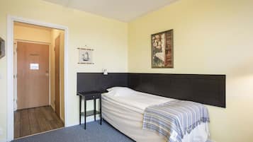 Una cama individual con cabecera oscura, una mesita de noche, un cuadro en la pared y una puerta que da a otra habitación.