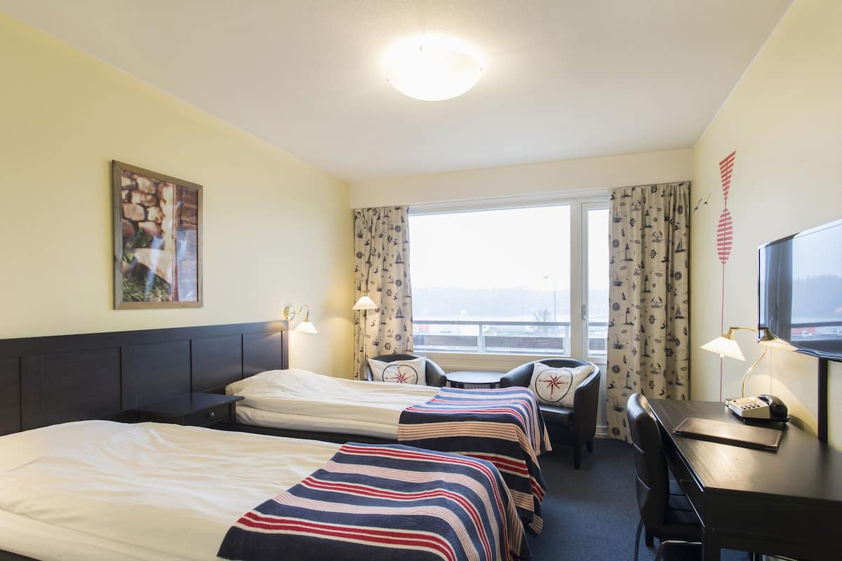 A hotel room with two beds, a desk, a chair, a TV, and a window with curtains.