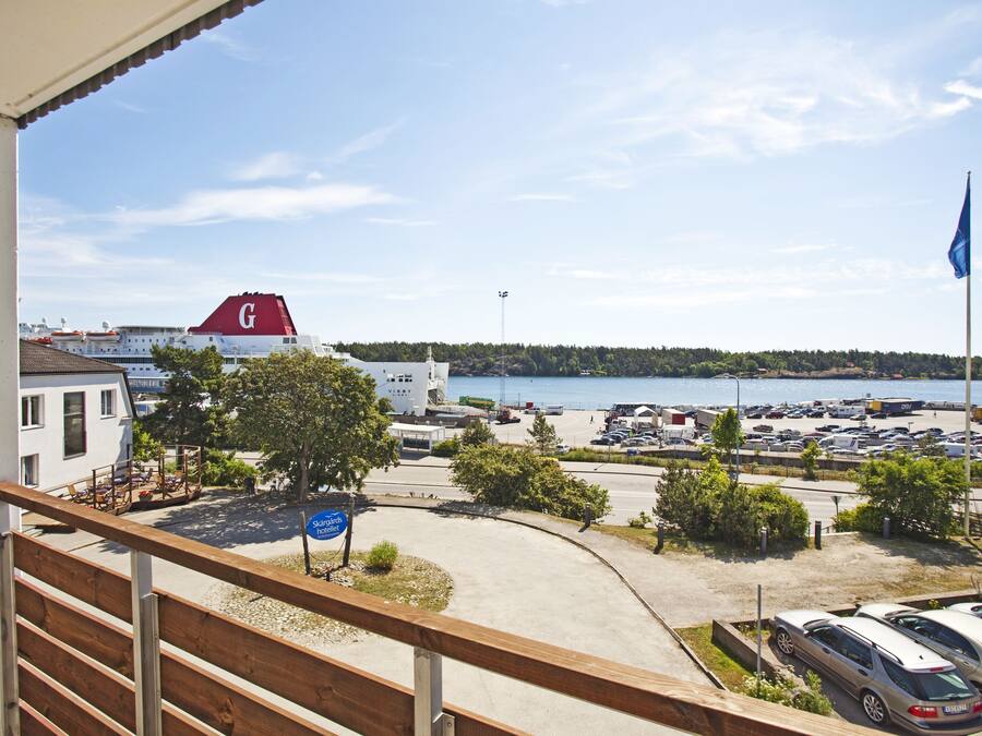 A view from a balcony overlooking a parking area with a body of water, a flag, and a building with a red 'G' on its roof.