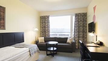 A hotel room with a bed, a sofa, a small round table, a desk with a chair, and a window with curtains.