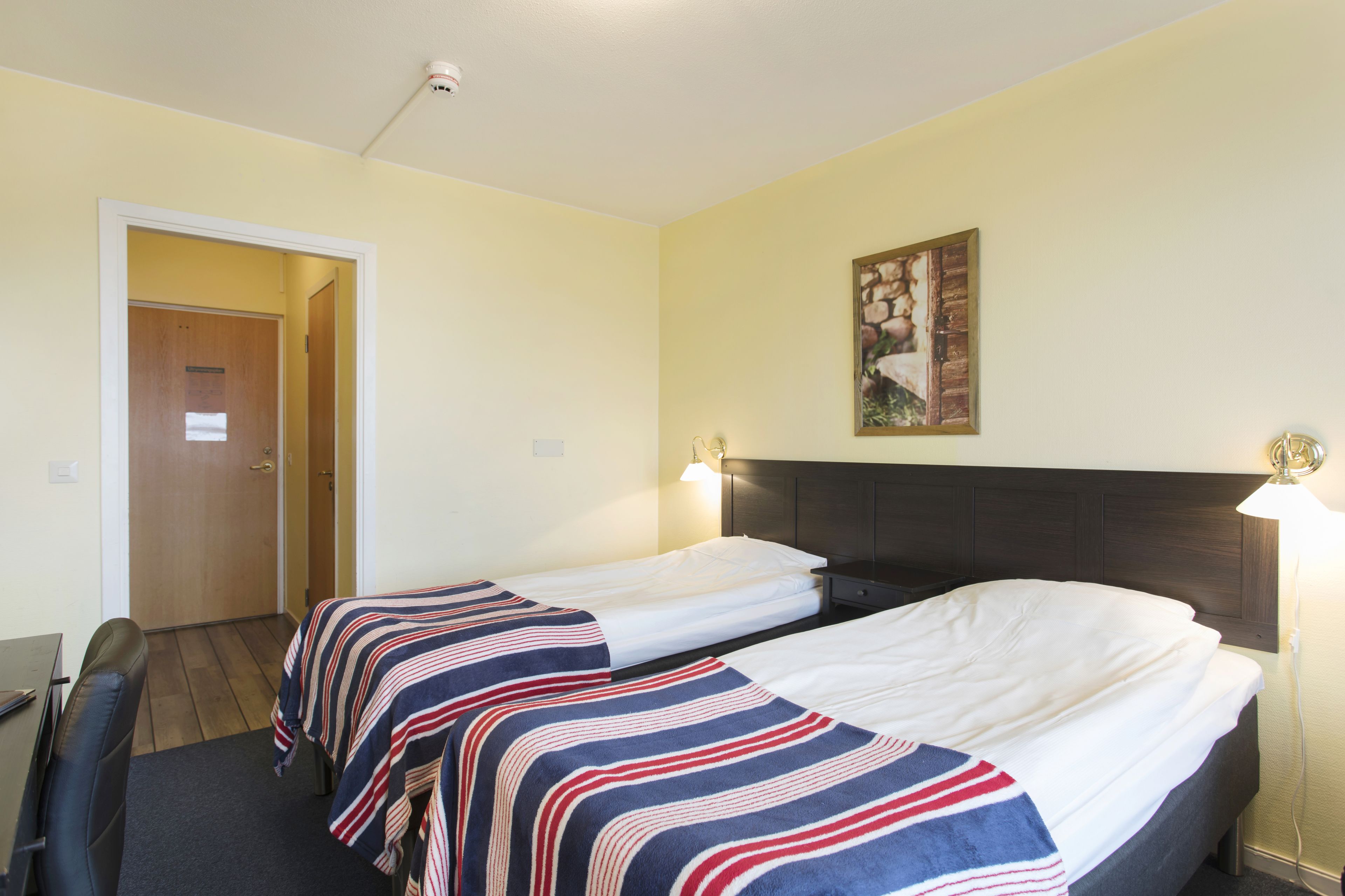 Ett hotellrum med två separata sängar, ett skrivbord och en stol.