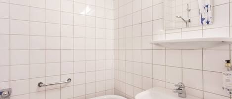 A bathroom with white tiles, a bathtub, a sink, and a mirror.