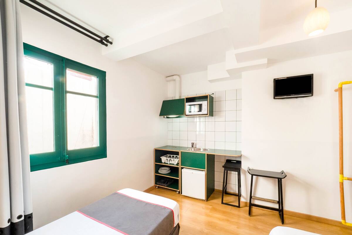 Una habitación compacta con dos camas, kitchenette, televisión y ventana.