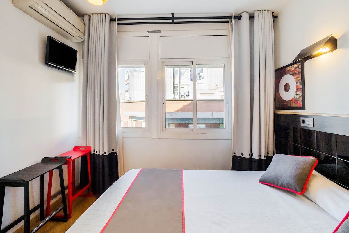 Habitación de hotel con cama, escritorio, televisor y ventana con cortinas.