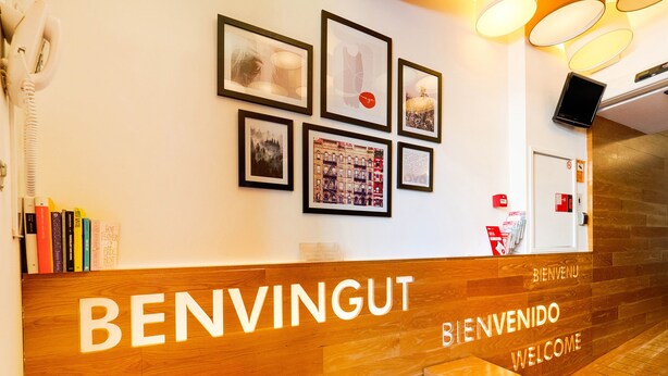 Una recepción con detalles de madera y las palabras "BENVINGUT" y "BIENVENIDO", lo que indica un entorno bilingüe.
