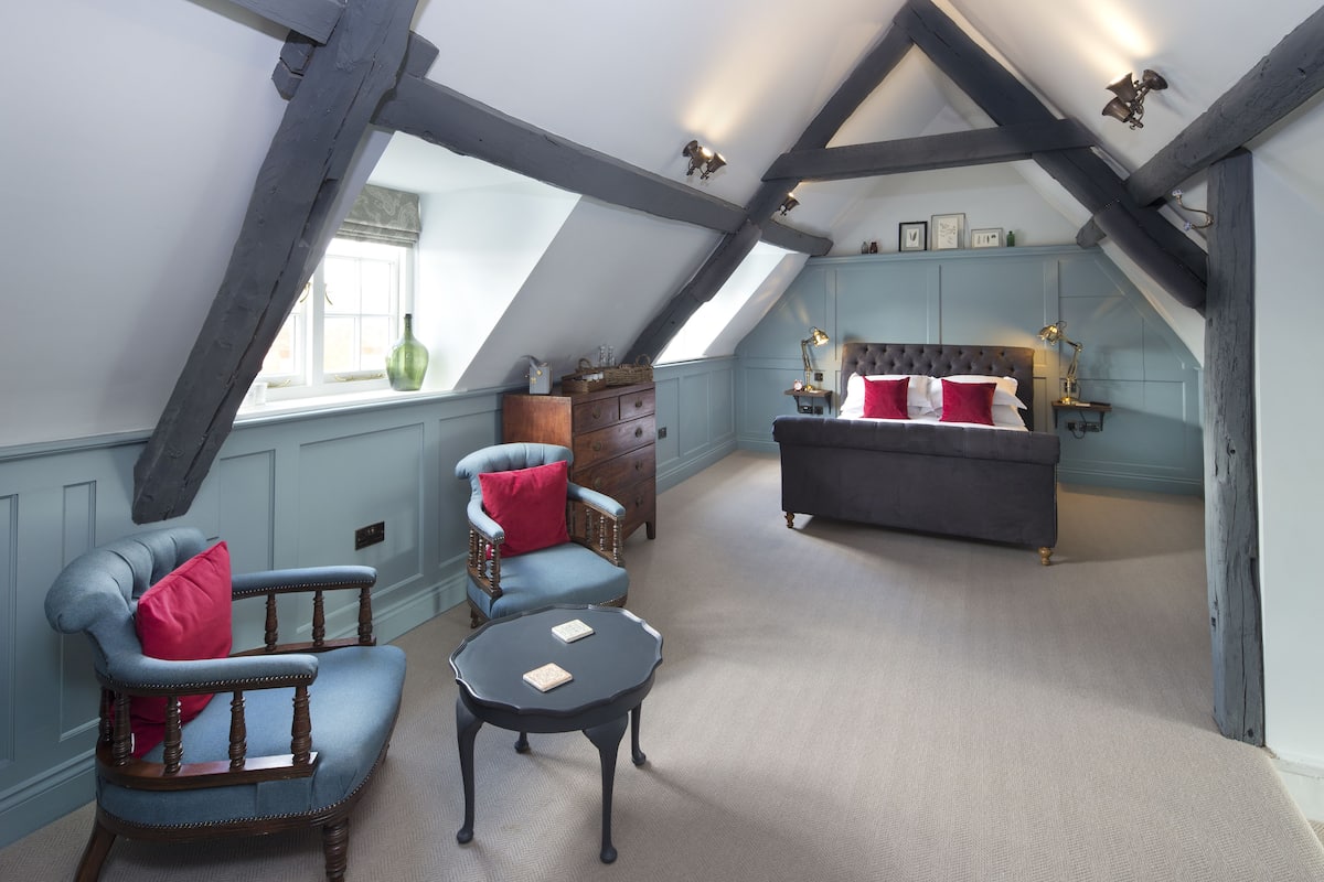 A cozy attic bedroom with a sloped ceiling, a large bed, a chair, a small table, and a dresser.