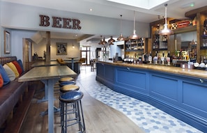 Uma área de bar com banquetas, um balcão de madeira e um letreiro que diz 'BEER'.