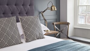 A neatly made bed with patterned pillows, a bedside lamp, and a wooden chair. - The George Townhouse (Shipston on Stour)