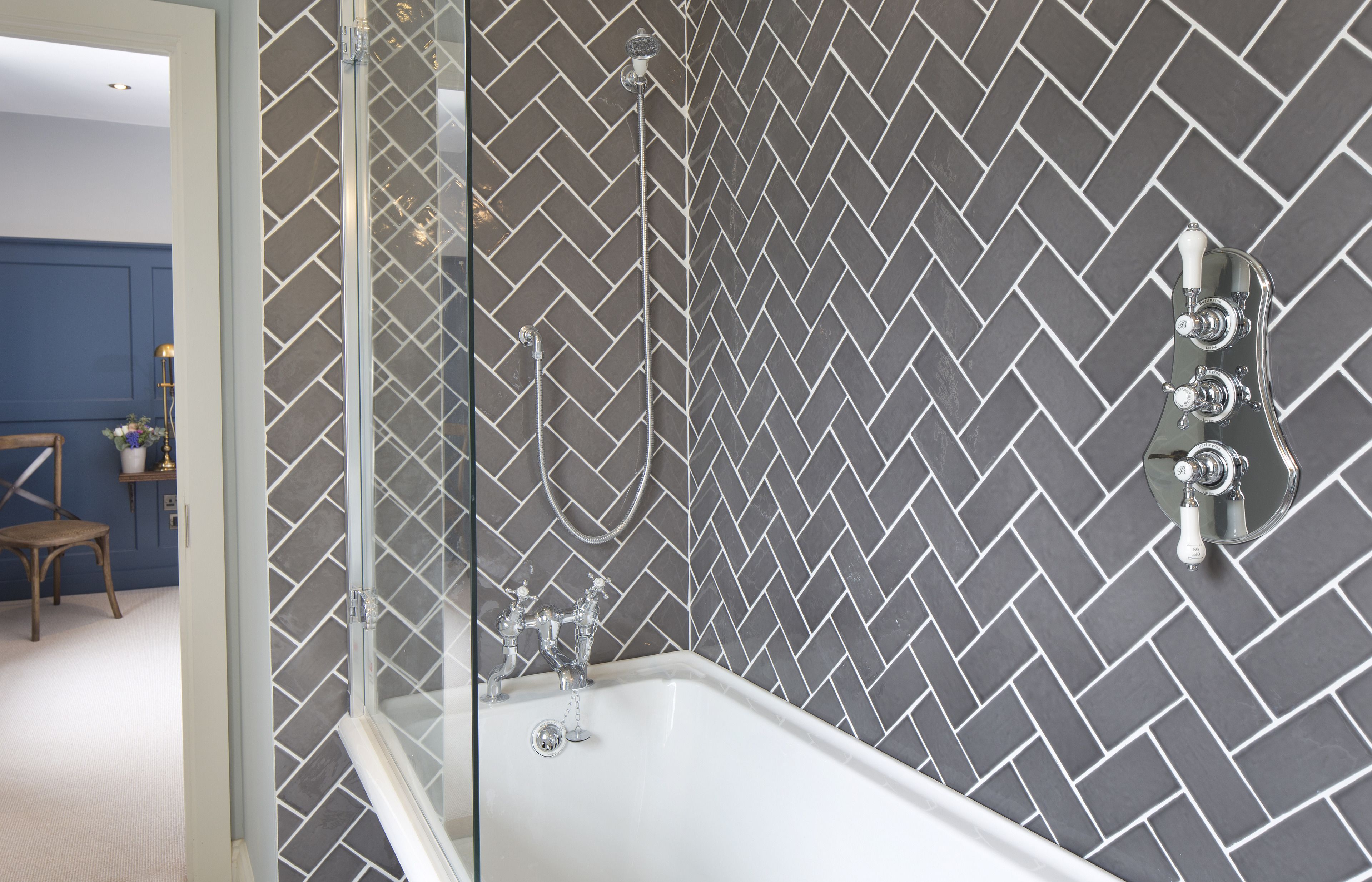 Een badkamer met een wand betegeld met een herringbonepatroon, een douche met glazen wanden en een wit bad.
