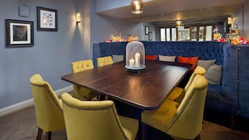Een eetgedeelte met een donker houten tafel, gele gestoffeerde stoelen en een blauwe gestoffeerde bank.