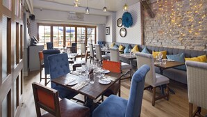 A restaurant with a stone wall, wooden furniture, and a view of the outside. - The George Townhouse (Shipston on Stour)