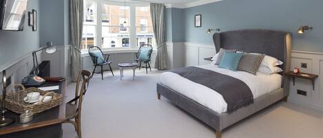 A bedroom with a large bed, a desk with a lamp, a chair, and a window with curtains.
