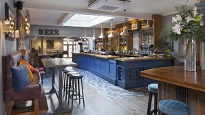 A bar area with a blue bar counter, stools, and a large vase of flowers. - The George Townhouse (Shipston on Stour)