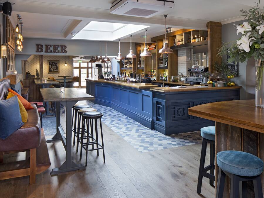 A bar area with a blue bar counter, stools, and a large vase of flowers.