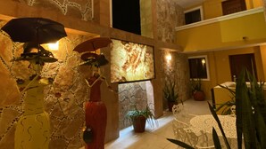 Un vestíbulo amplio con techo alto, paredes de piedra y lámparas modernas. Hay plantas en macetas y una zona de estar con una mesa y sillas.